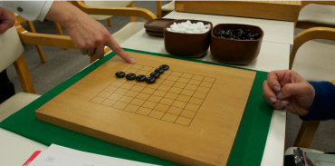 テキストと進行表入りのマイファイルをもらい、レッツレッスン！　勝負は“地（じ）”と呼ばれる陣地の多い方が勝つ、線と線の交点に石を置くなど囲碁のマナーとルールを理解。（イメージ）